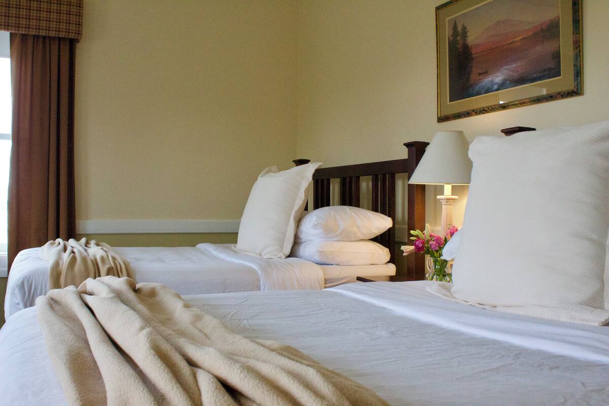 A hotel room with two beds, a nightstand with a lamp, and a painting on the wall.