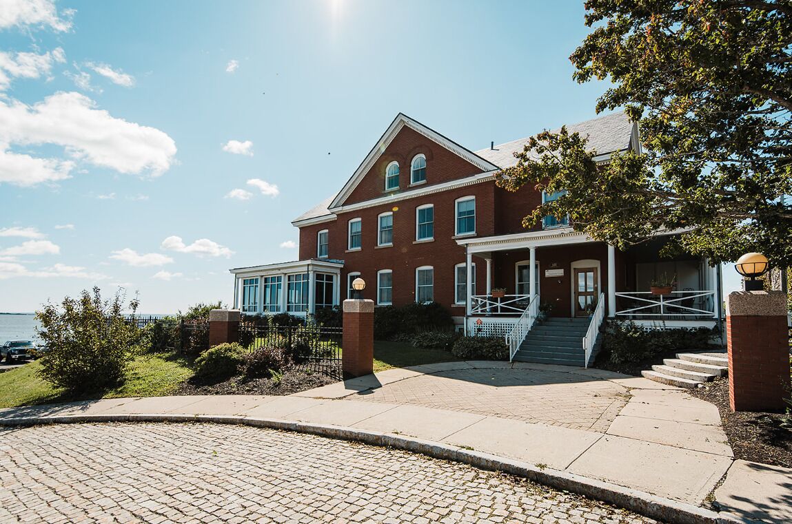 A large brick building with a porch and steps leading to the entrance.