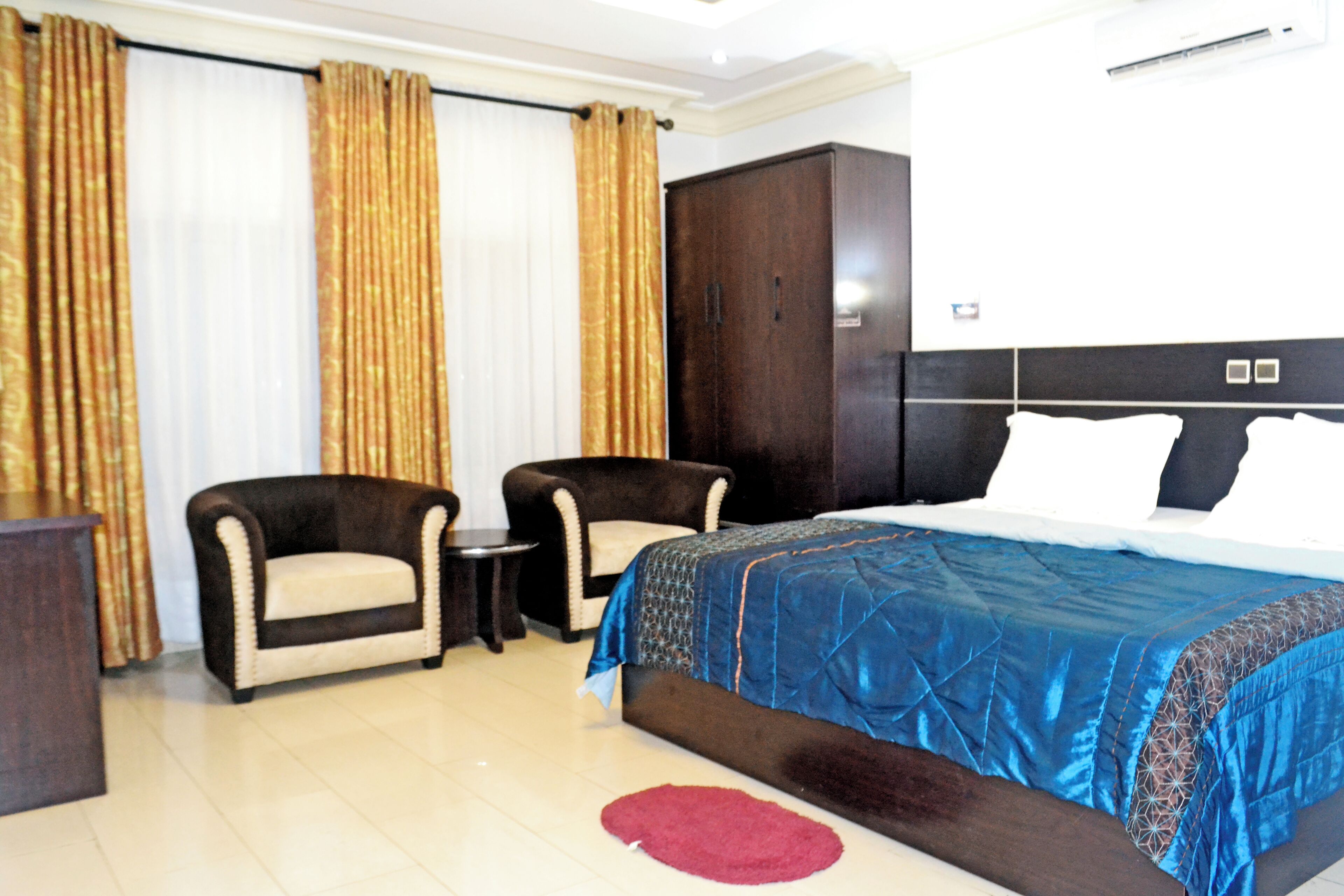 Habitación de hotel con una cama grande, dos sillones, una mesita, un armario y una alfombra roja.