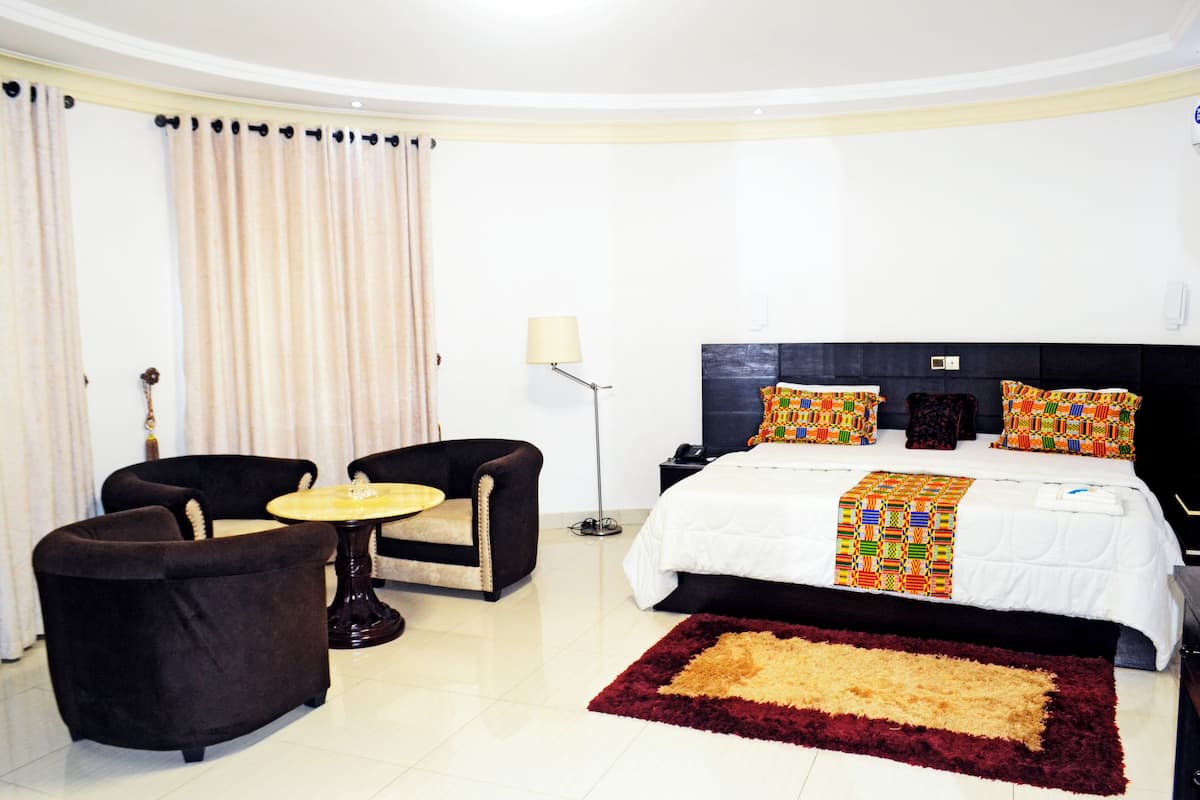 Une chambre d’hôtel comprenant un lit, deux fauteuils, une petite table ronde, une lampe sur pied et un grand tapis.