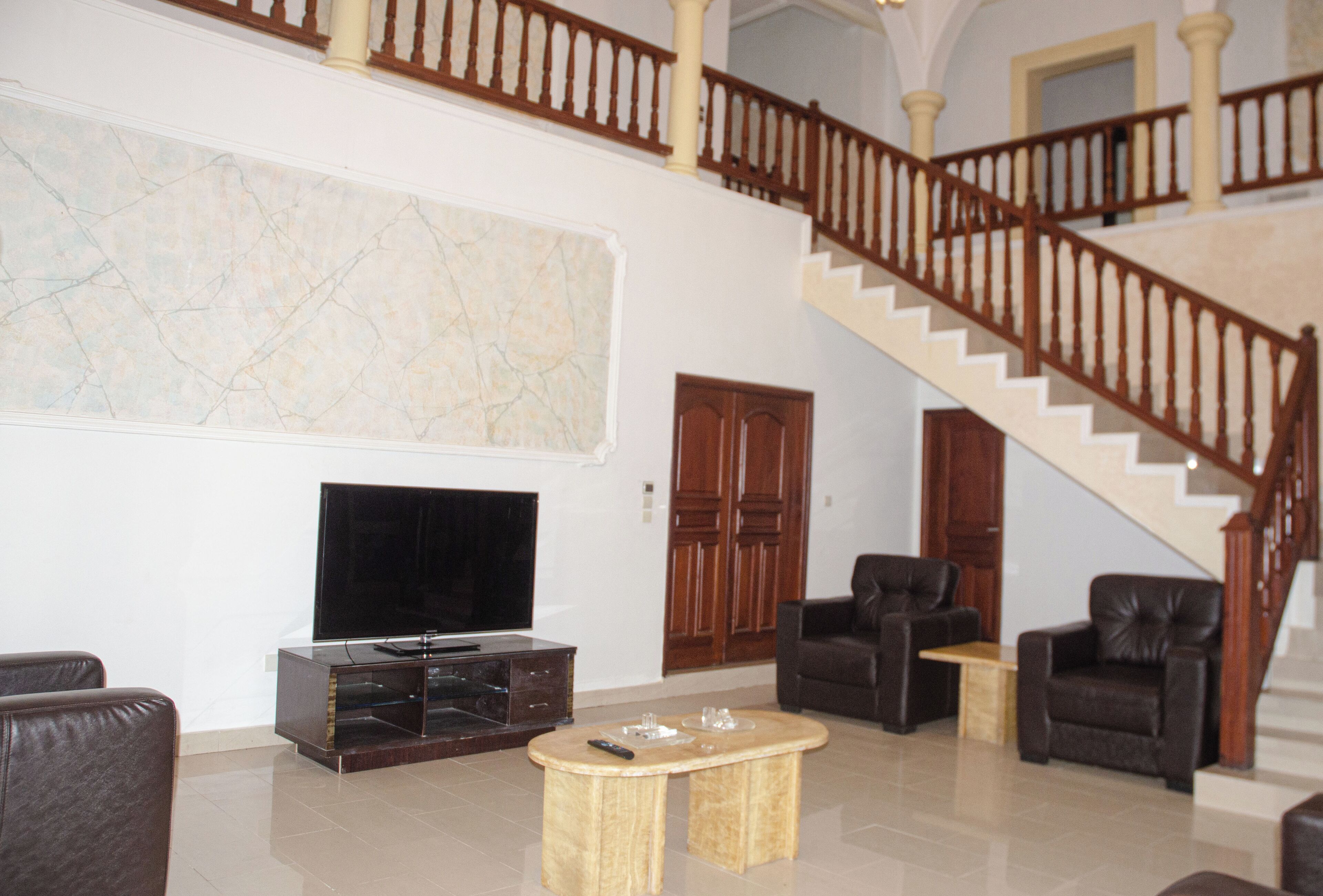 A spacious living room with a large TV, leather sofas, a wooden coffee table, and a grand staircase.