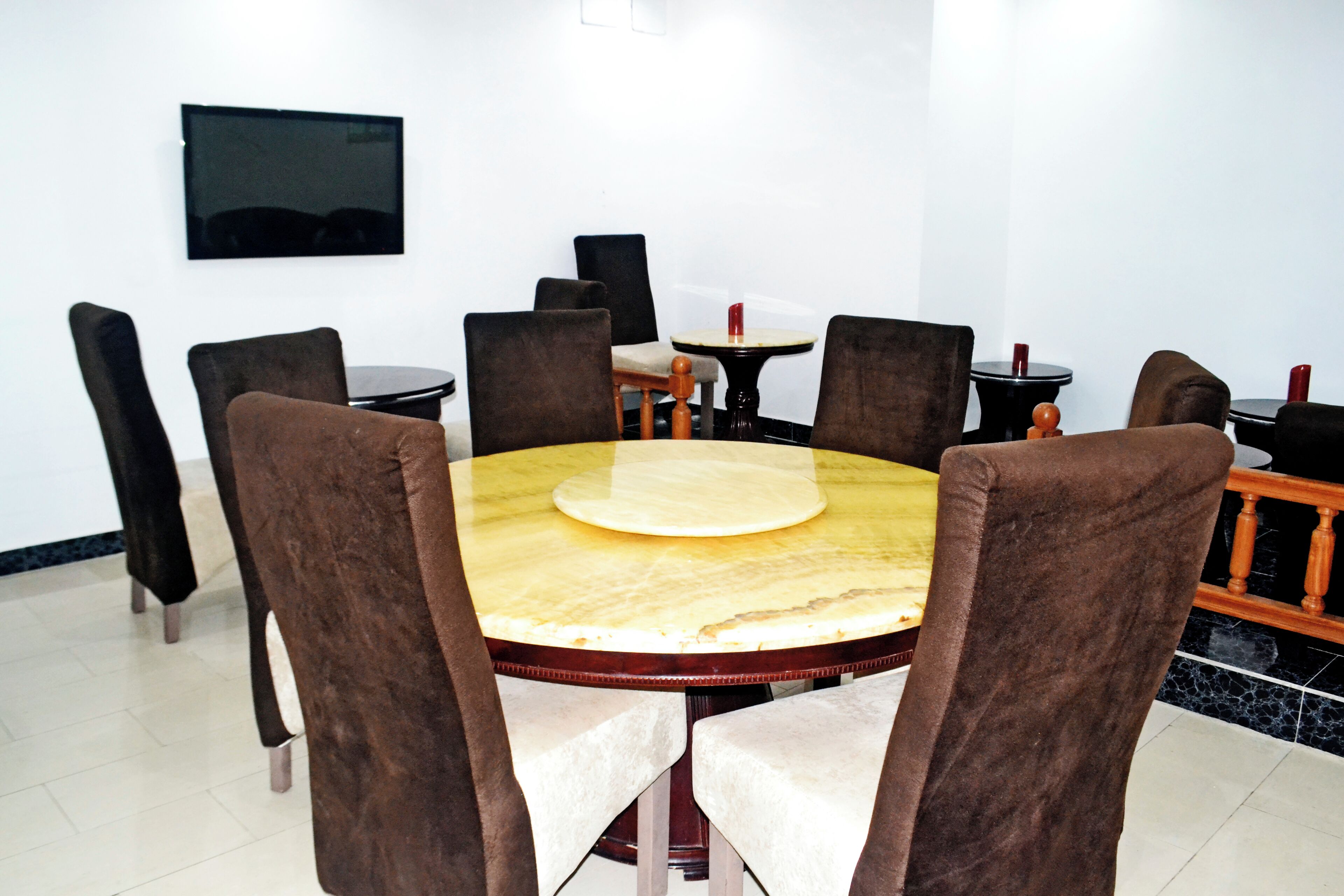 Un comedor con una mesa redonda, sillas tapizadas en tono café, una mesita redonda con una vela roja y un televisor de pantalla plana montado en la pared.