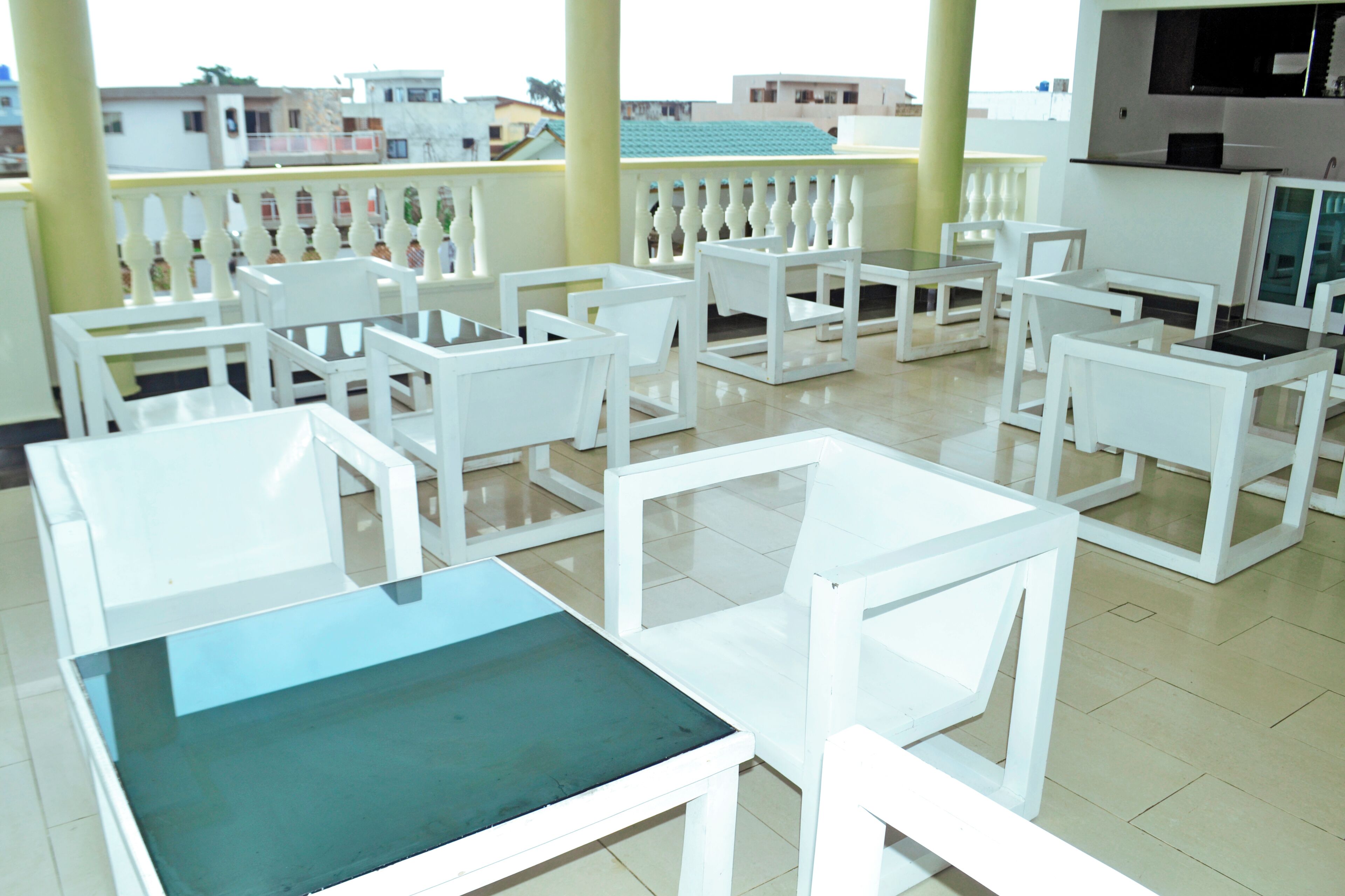Habitación de hotel con muebles blancos, un balcón con barandilla y vistas a edificios.