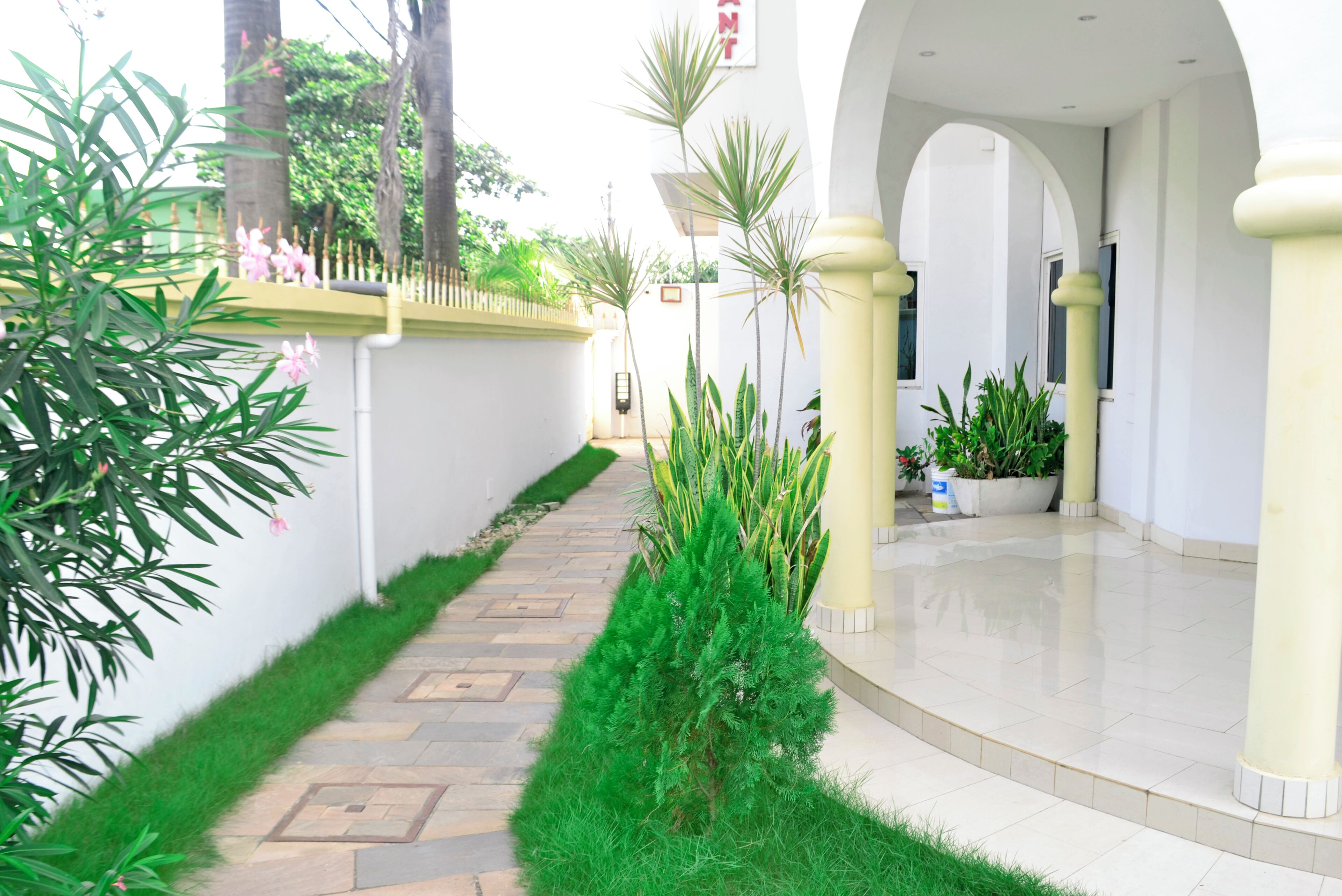 A clean, well-maintained indoor pathway with a tiled floor, surrounded by greenery and white walls.