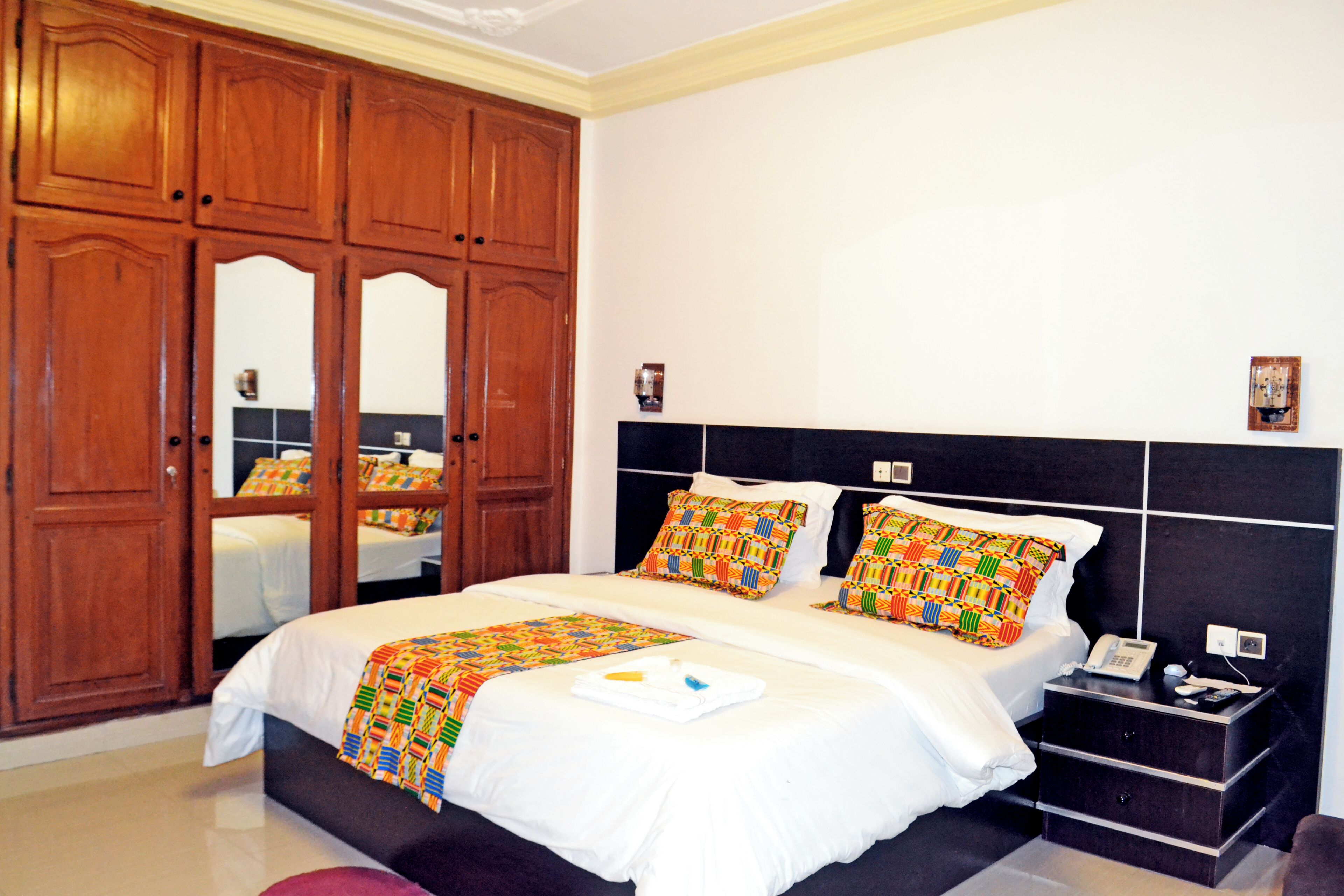 Una habitación de hotel con una cama grande, un armario de madera, una mesita de noche y una mesita auxiliar.