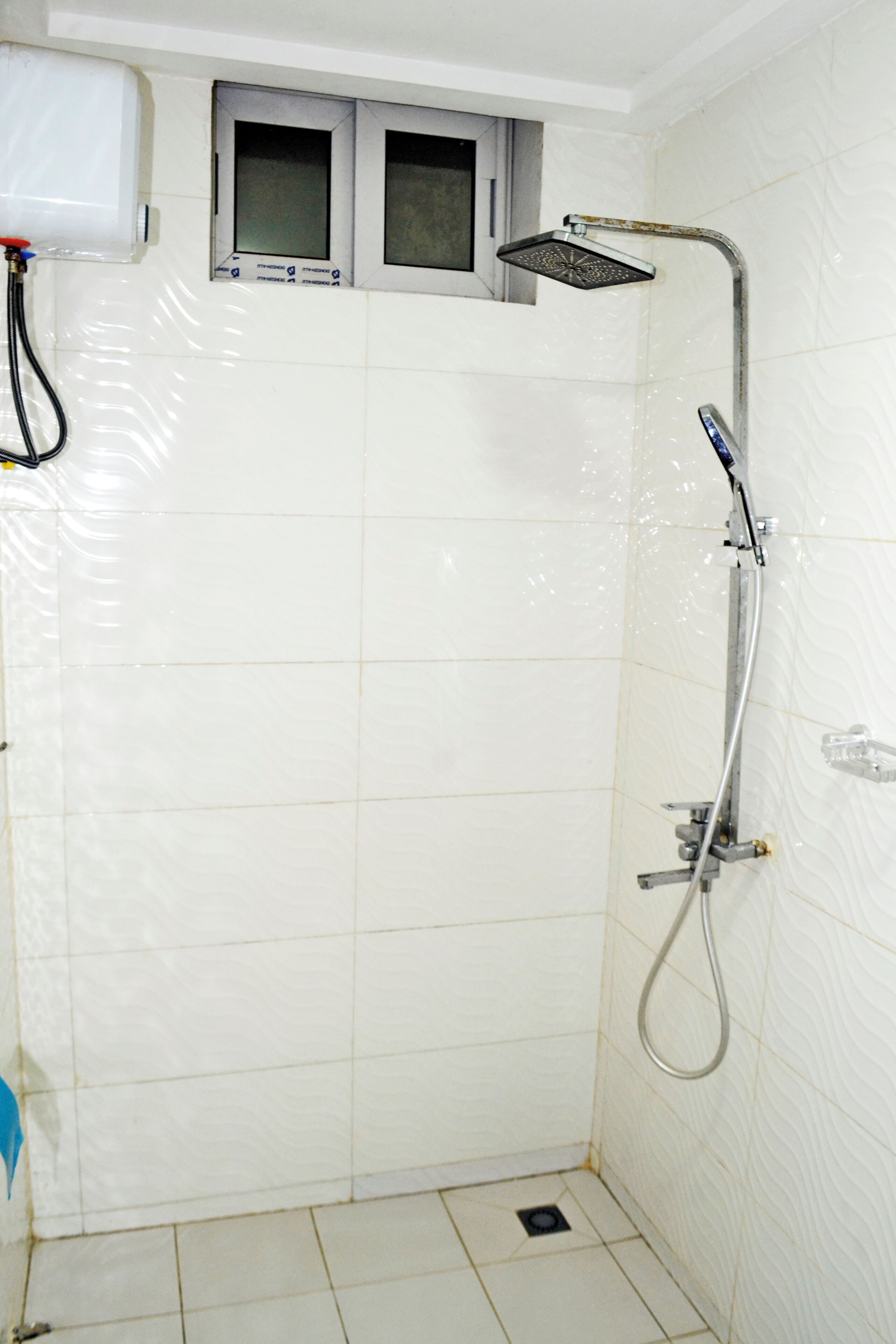 A small, tiled shower room with a handheld showerhead and a wall-mounted faucet.