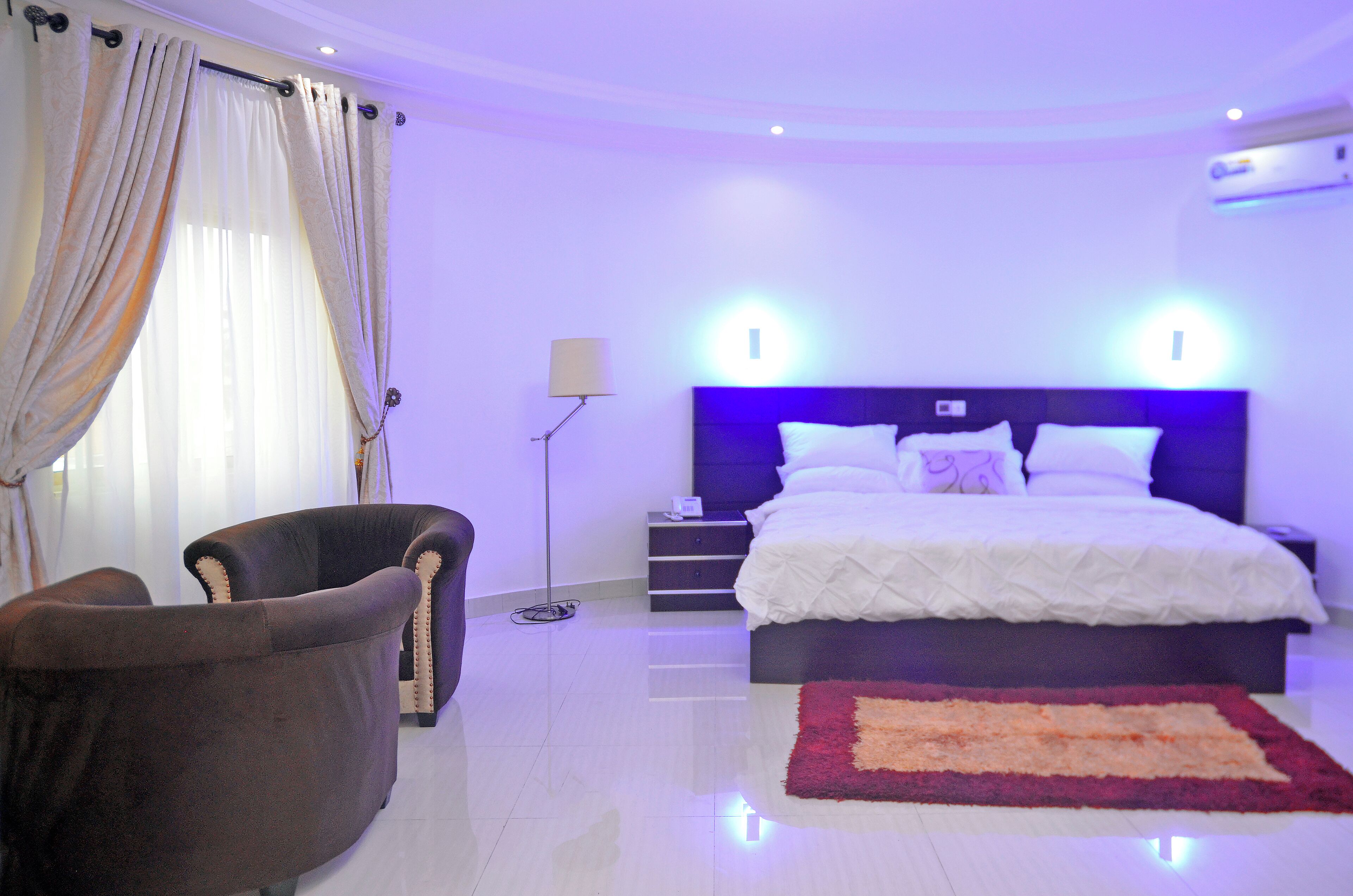 A bedroom with a bed, a chair, a bedside table, and a floor lamp.
