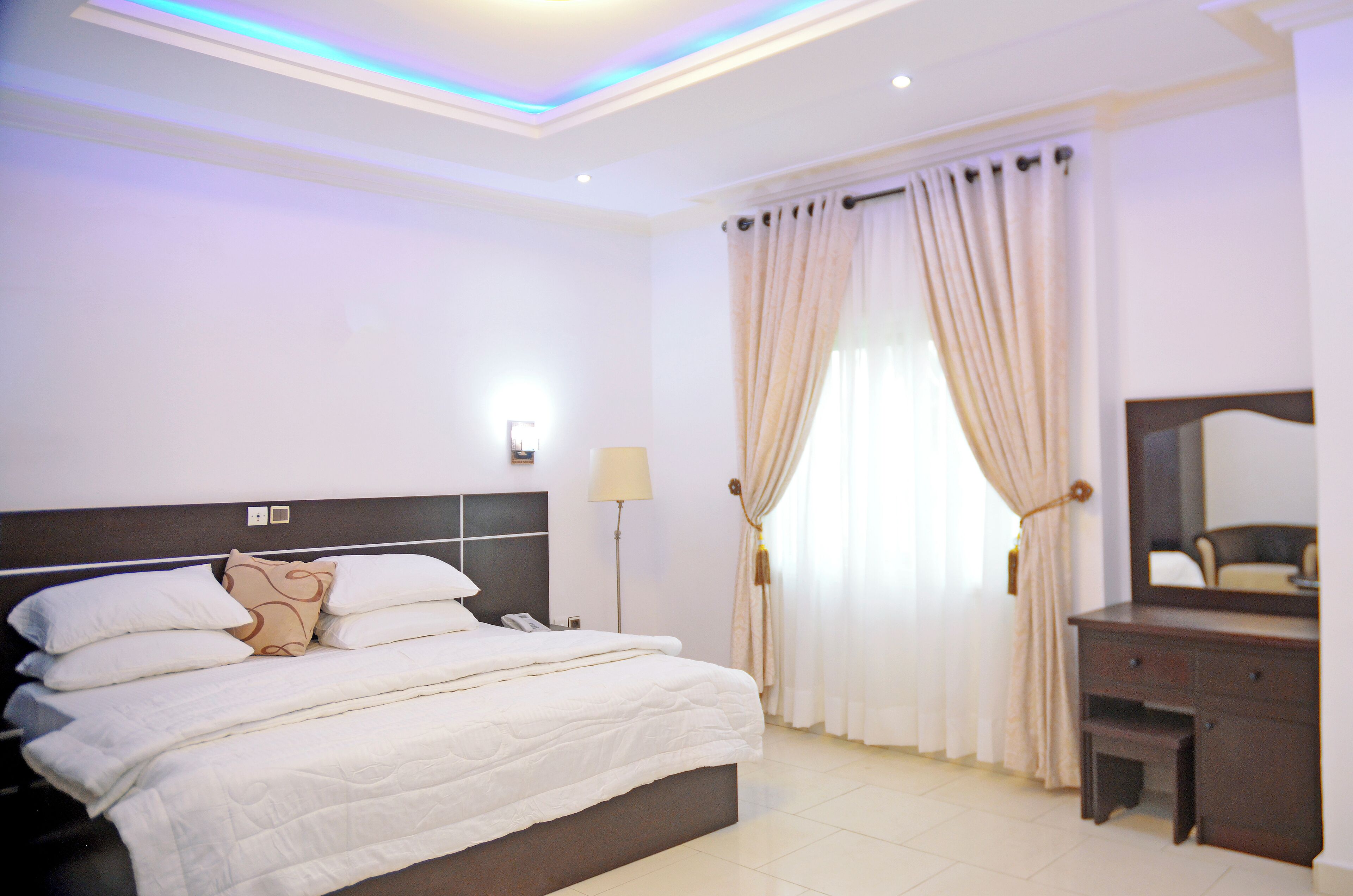 A hotel room with a large bed, a bedside table, a mirror, and a window with curtains.
