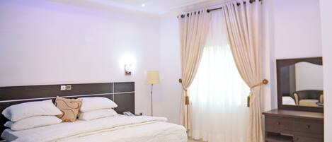 A hotel room with a large bed, a bedside table, a mirror, and a window with curtains.