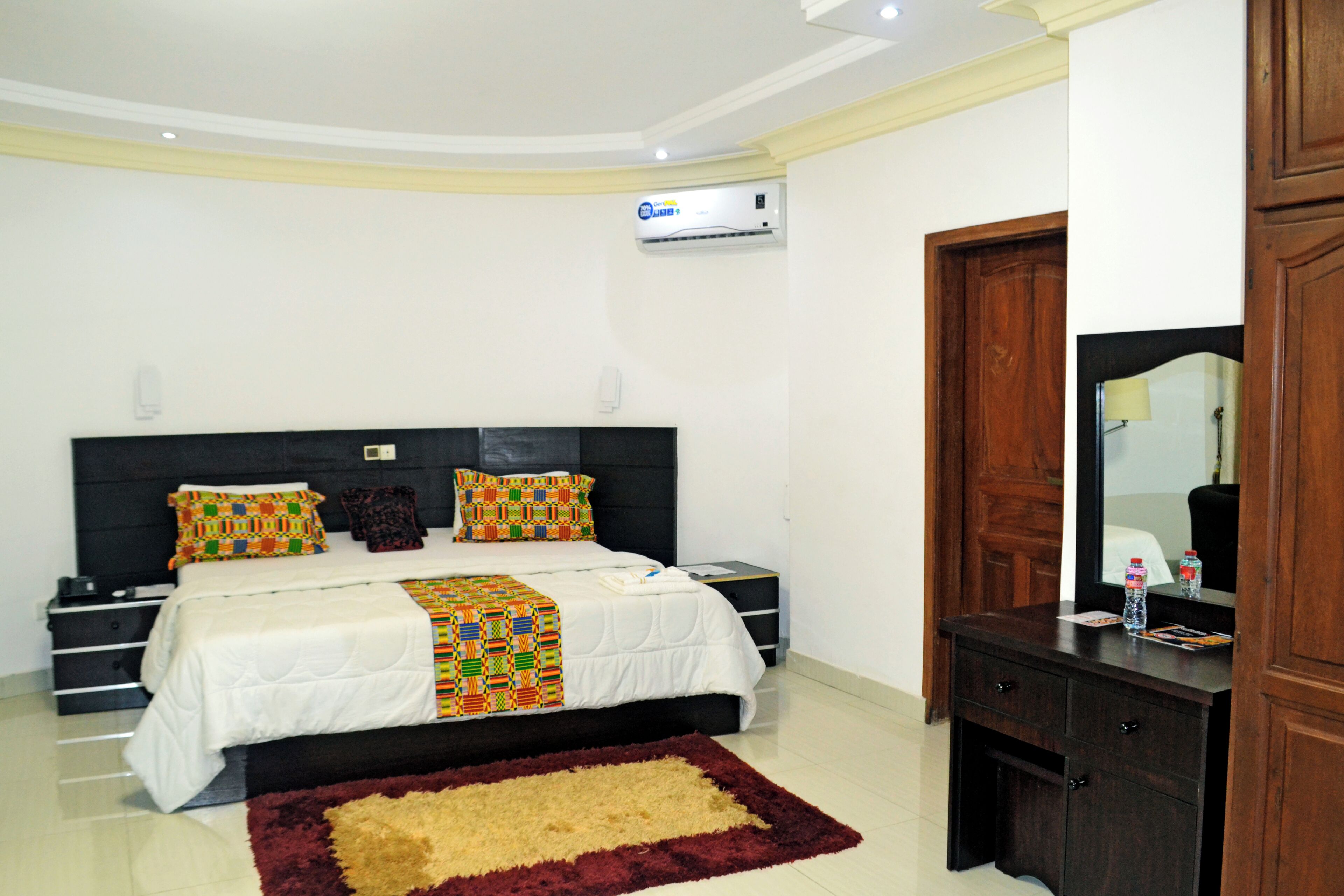 A bedroom with a bed, bedside tables, a dresser, a mirror, and an air conditioning unit.