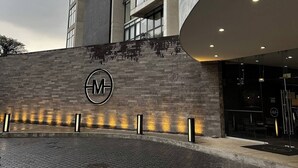A modern building with a prominent logo on the facade, a paved entrance area, and a glass entrance. - Adorable 1-bedroom apartment in tranquil Queretaro perfect for relaxing (QUERETARO)