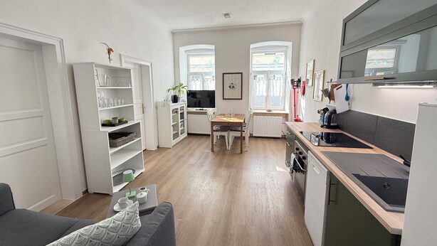 A modern kitchen with a dining area, built-in shelving, and a large window providing natural light.