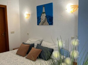Un dormitorio con cama, almohadas, un cuadro y apliques de pared.