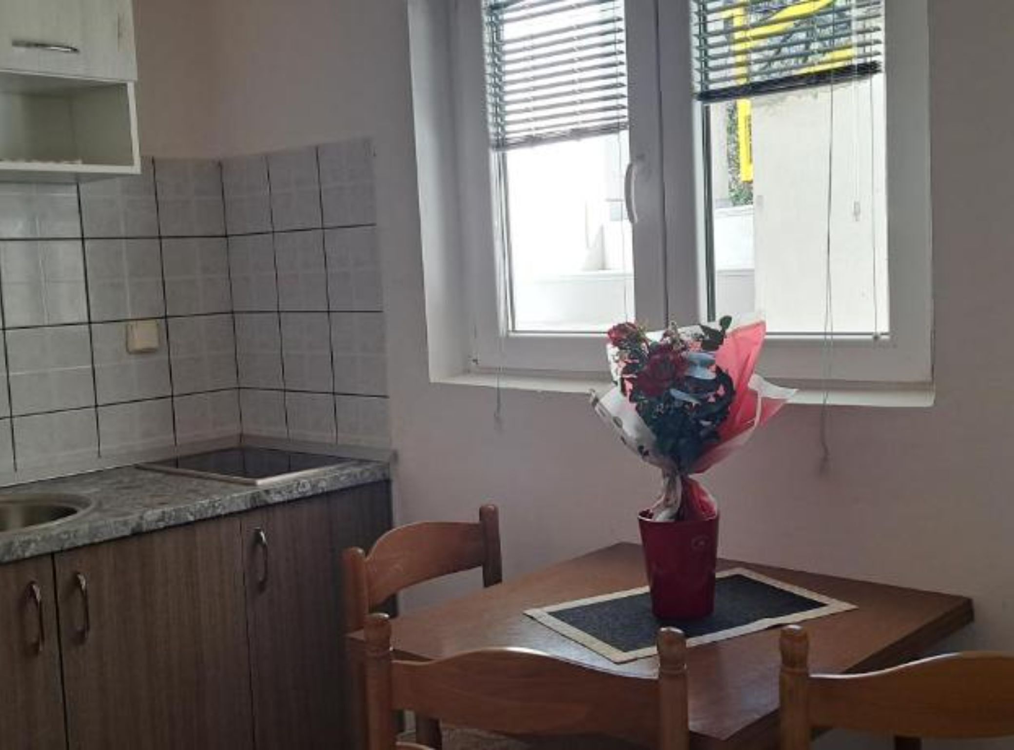A kitchen with a window, a dining table with chairs, and a bouquet of flowers on the table.