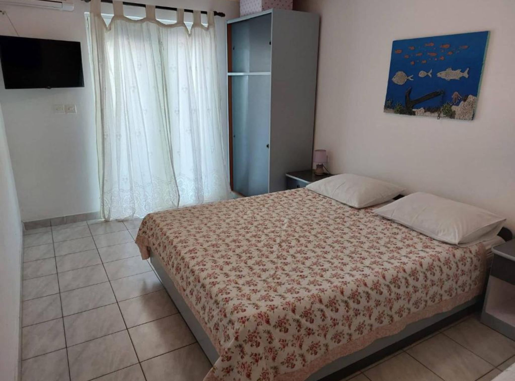 A bedroom with a bed, a wardrobe, a TV, and a painting on the wall.