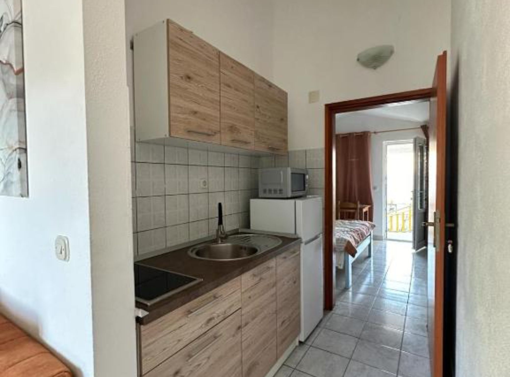 Una cocina compacta con armarios de madera, un microondas y un lavamanos.