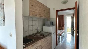 Una cocina compacta con armarios de madera, un microondas y un lavamanos.