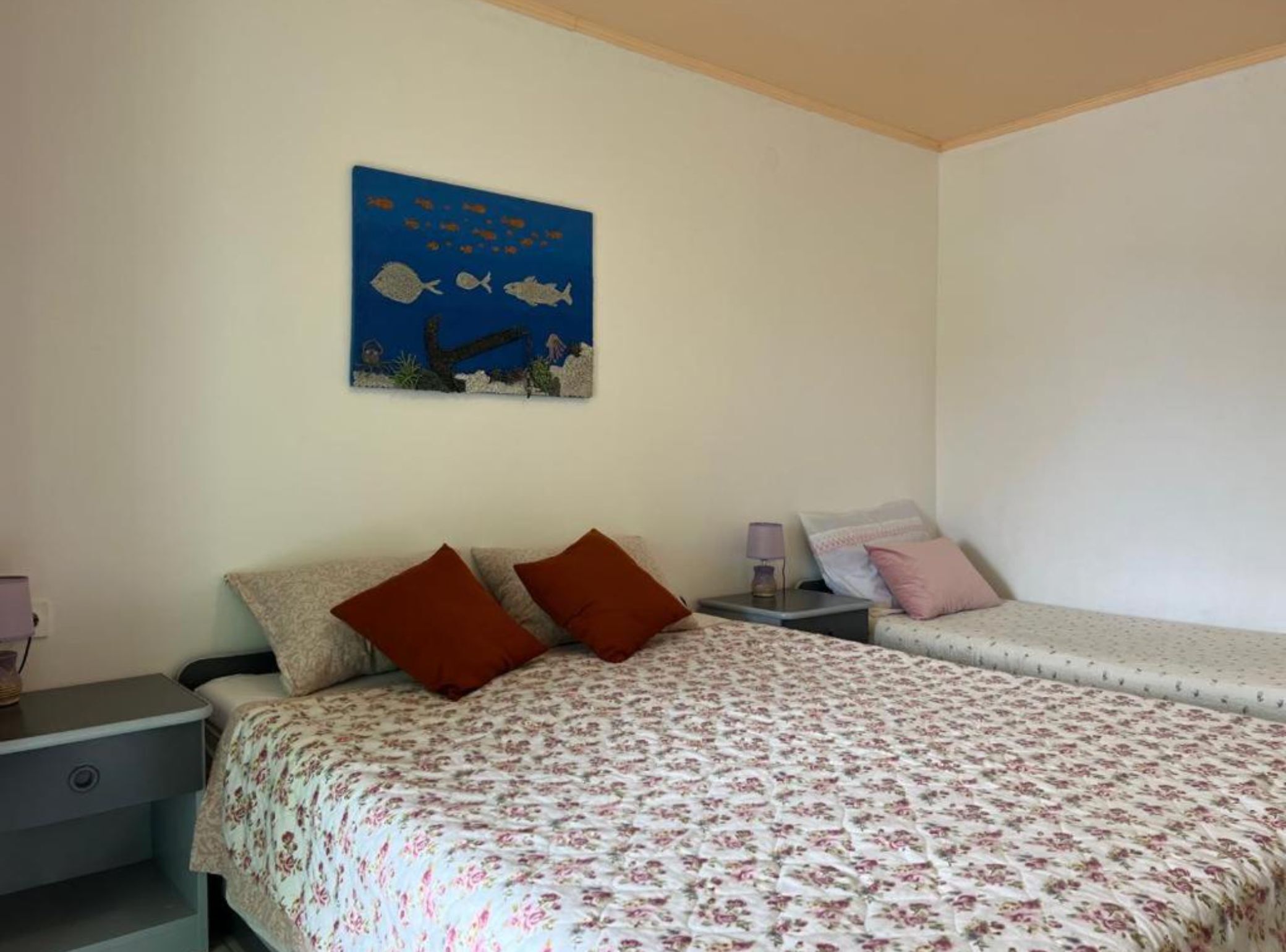 Un dormitorio con dos camas, una mesita de noche, una lámpara y un cuadro de peces en la pared.