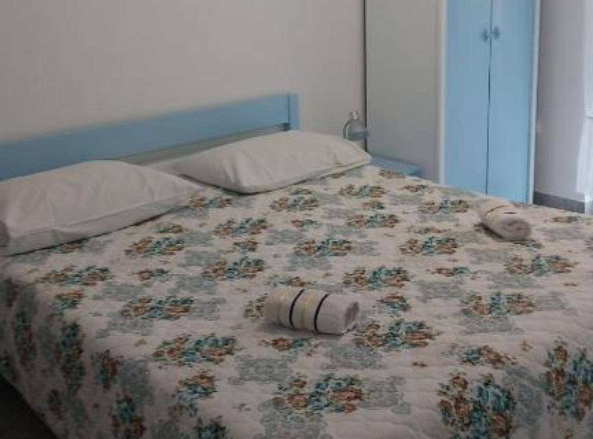 Una cama con ropa de cama floral, un cabecero azul y una almohada blanca.