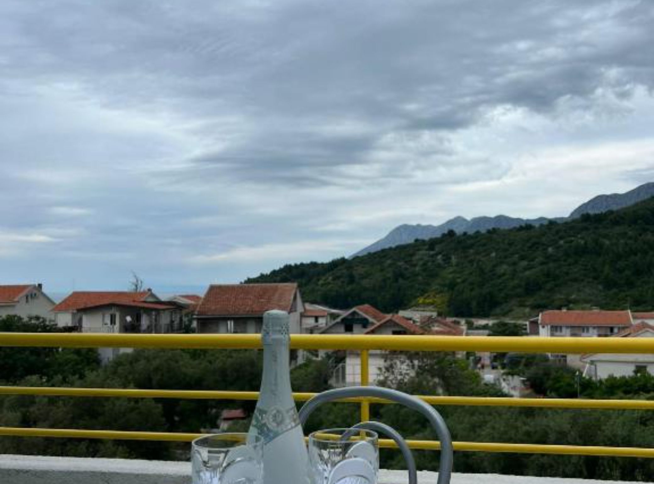Mesa con una botella y vasos, con vista a una zona residencial con casas y montañas.