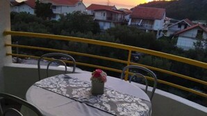 A balcony with a table and chairs, overlooking a residential area with houses and a mountain in the background. - Apartments Natali (Gradac)