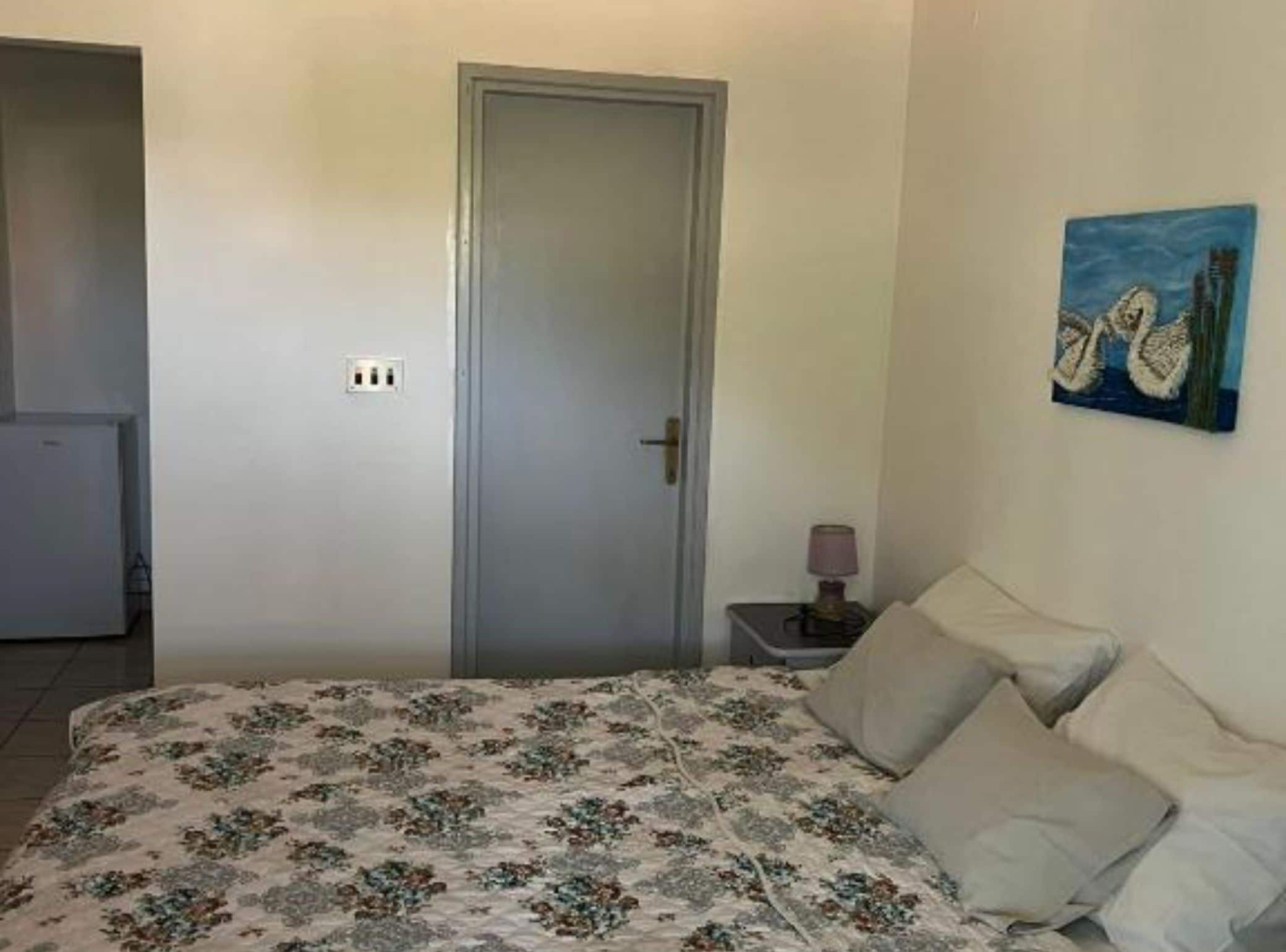 Ein Schlafzimmer mit Bett, Tür, Nachttisch mit Lampe und einem Bild an der Wand.