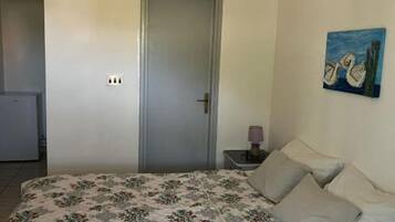 Ein Schlafzimmer mit Bett, Tür, Nachttisch mit Lampe und einem Bild an der Wand.