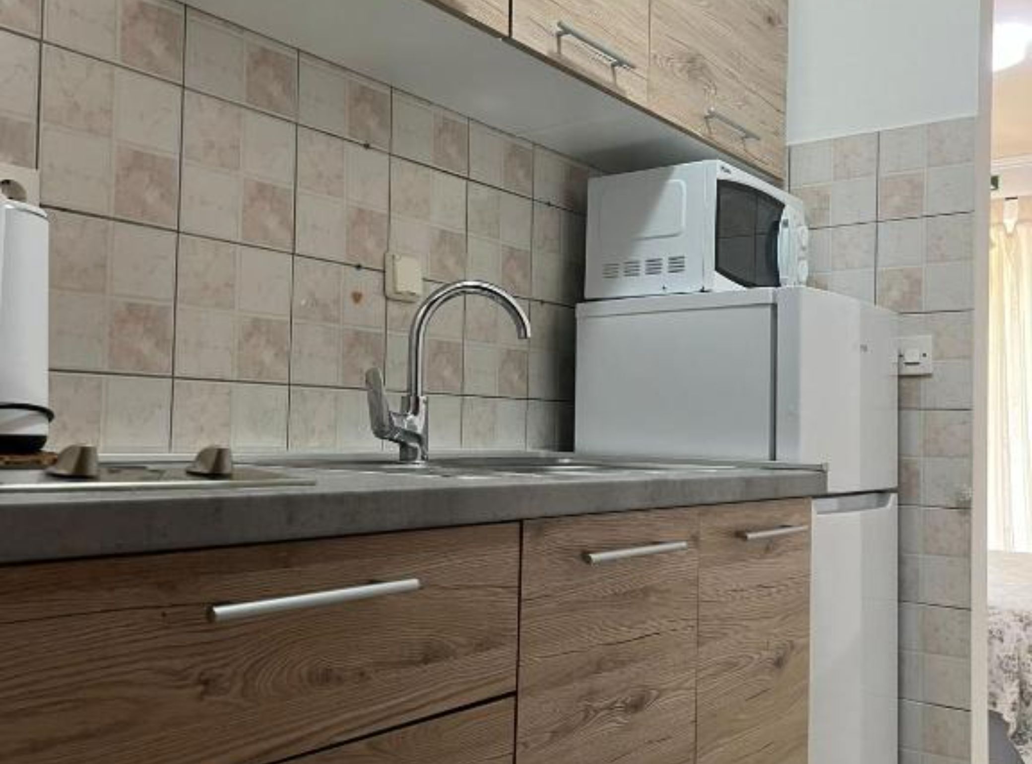 A kitchen with a tiled backsplash, a stainless steel sink, a microwave, and wooden cabinets.