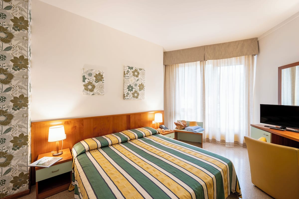 Una habitación de hotel con cama, lámparas de noche, televisión y escritorio.