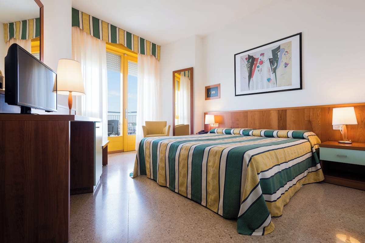 Habitación de hotel con una cama grande, televisión, escritorio con lámpara y ventana con cortinas.