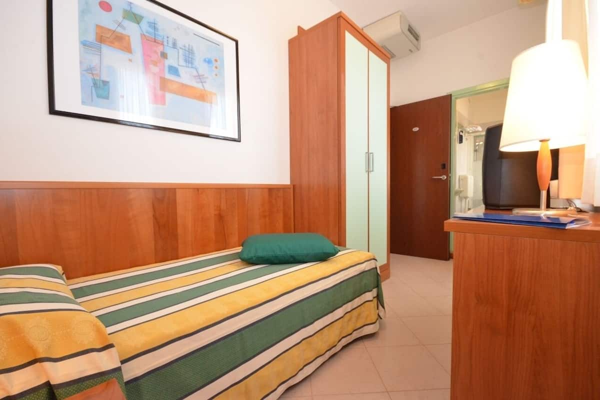 Una habitación con cama, un armario de madera, un escritorio con lámpara y un cuadro en la pared.