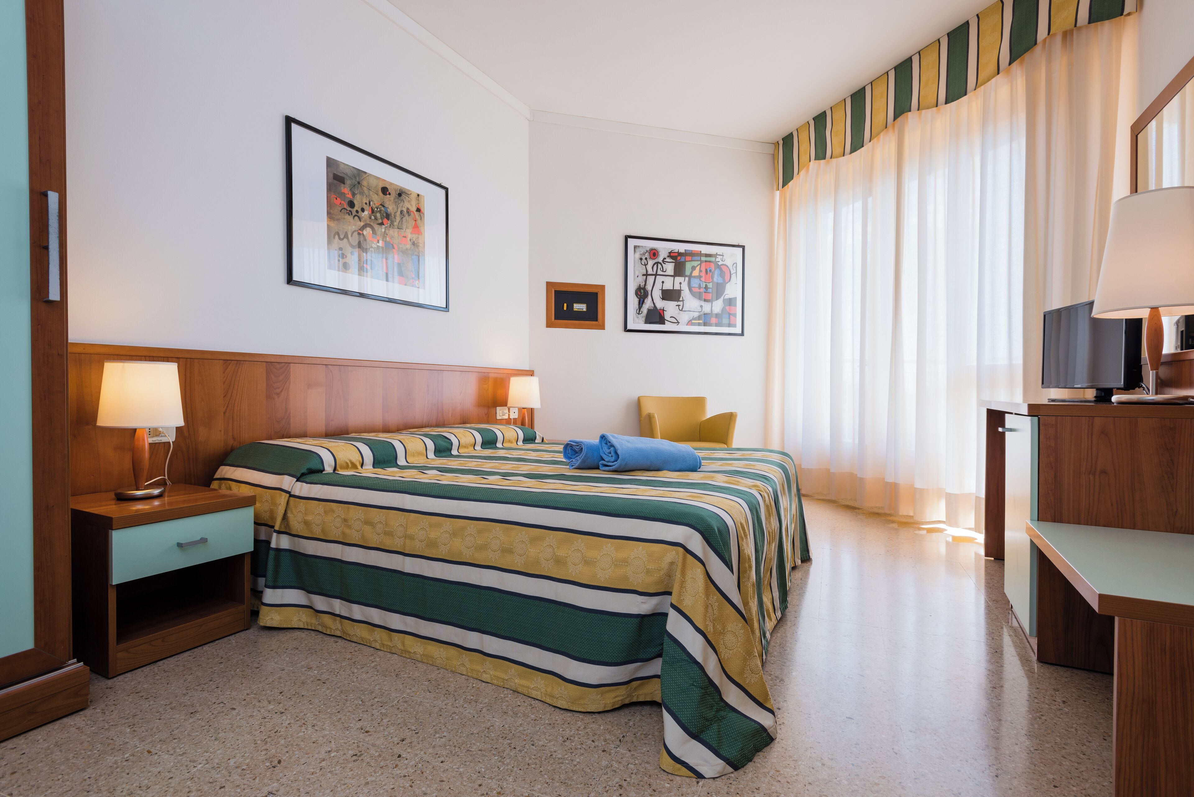 A hotel room with a bed, two bedside tables, a chair, a desk, and a television.