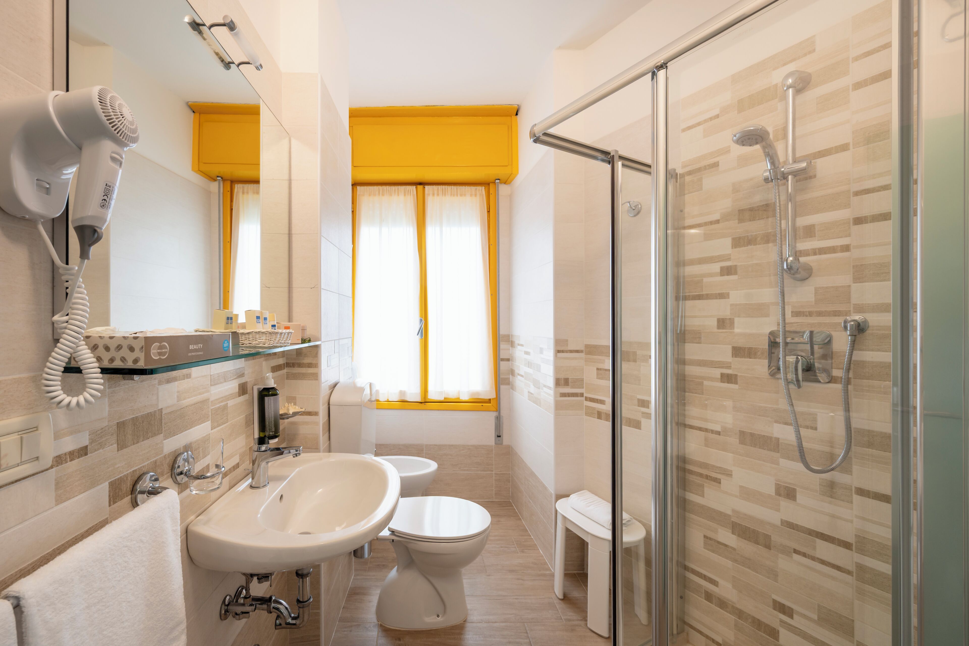A bathroom with a glass shower enclosure, a hairdryer, a sink, and a toilet.