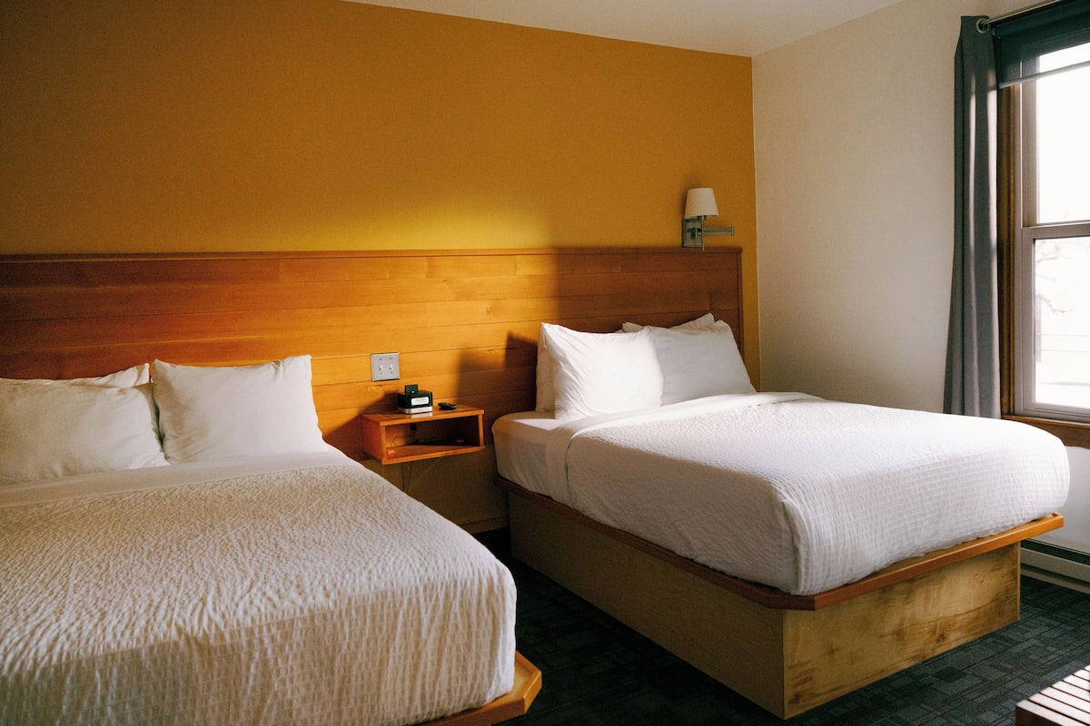 Two single beds with wooden headboards, a nightstand with a lamp, and a window with curtains.
