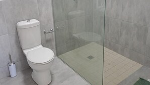 Un baño con inodoro, ducha envuelta en vidrio y suelo de baldosas.