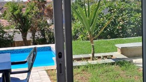 Vista desde un balcón sobre una piscina, un área verde y una playa, con cielo despejado.