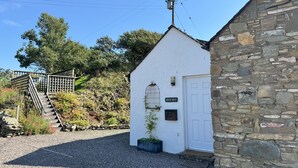 A white building with a stone extension, a wooden staircase, and a sign reading "Birds Nest". - Birds Nest -  a cottage that sleeps 2 guests  in 1 bedroom (Gatehouse of Fleet)