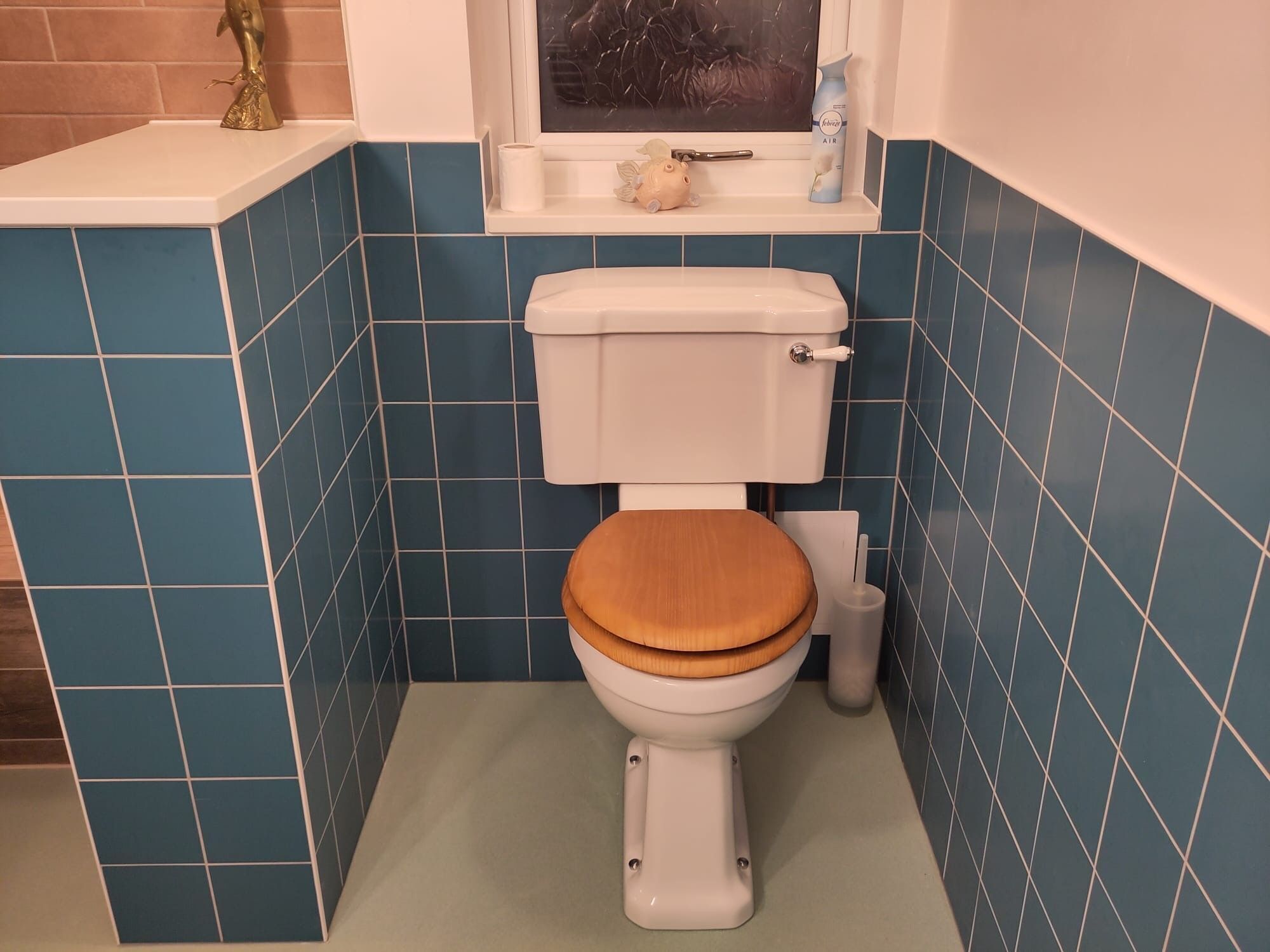 Een badkamer met een toilet, een raam en een plankje met een decoratief object en een fles.