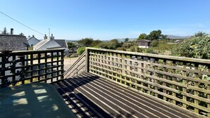 A wooden deck with a metal railing, leading to a residential area with houses and a clear view of the landscape. - Birds Nest -  a cottage that sleeps 2 guests  in 1 bedroom (Gatehouse of Fleet)