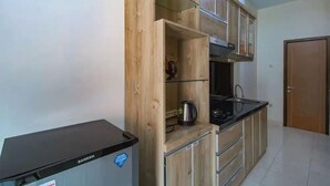A compact kitchen with wooden cabinets, a black countertop, and a stainless steel kettle.