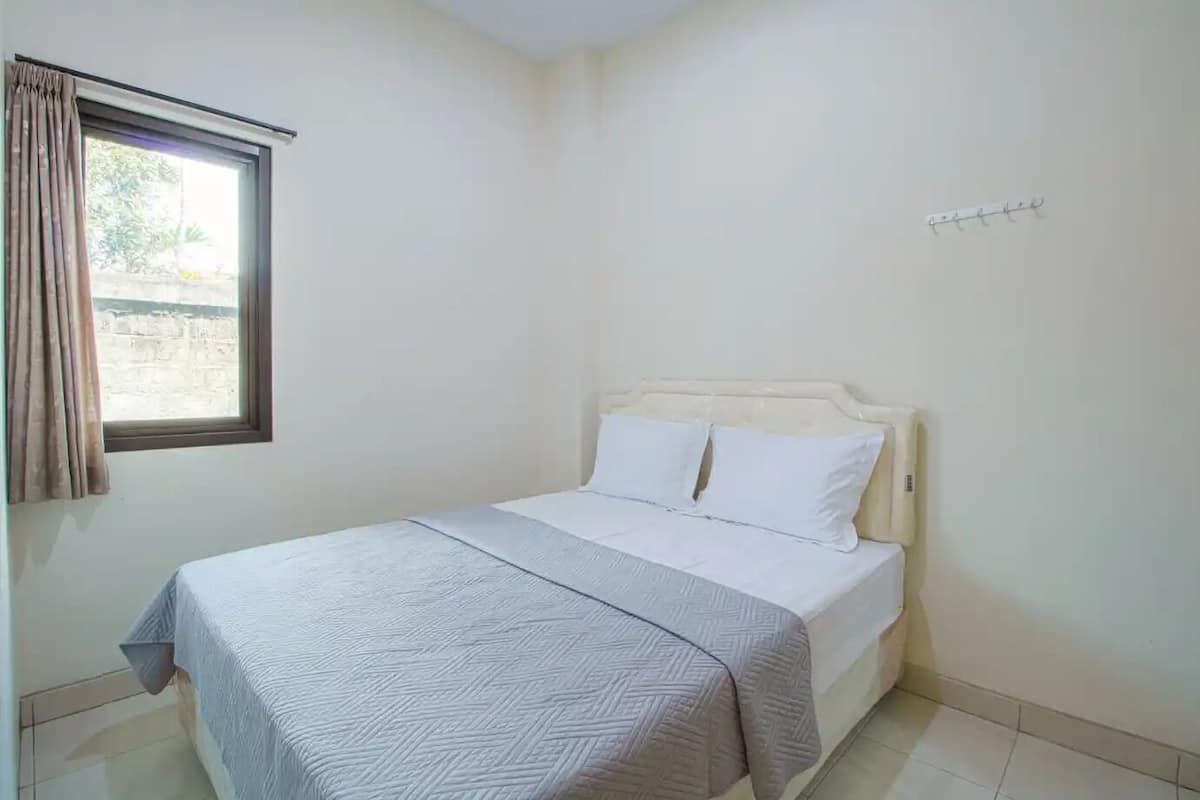 Une chambre avec un lit, une fenêtre avec des rideaux et un crochet fixé au mur.