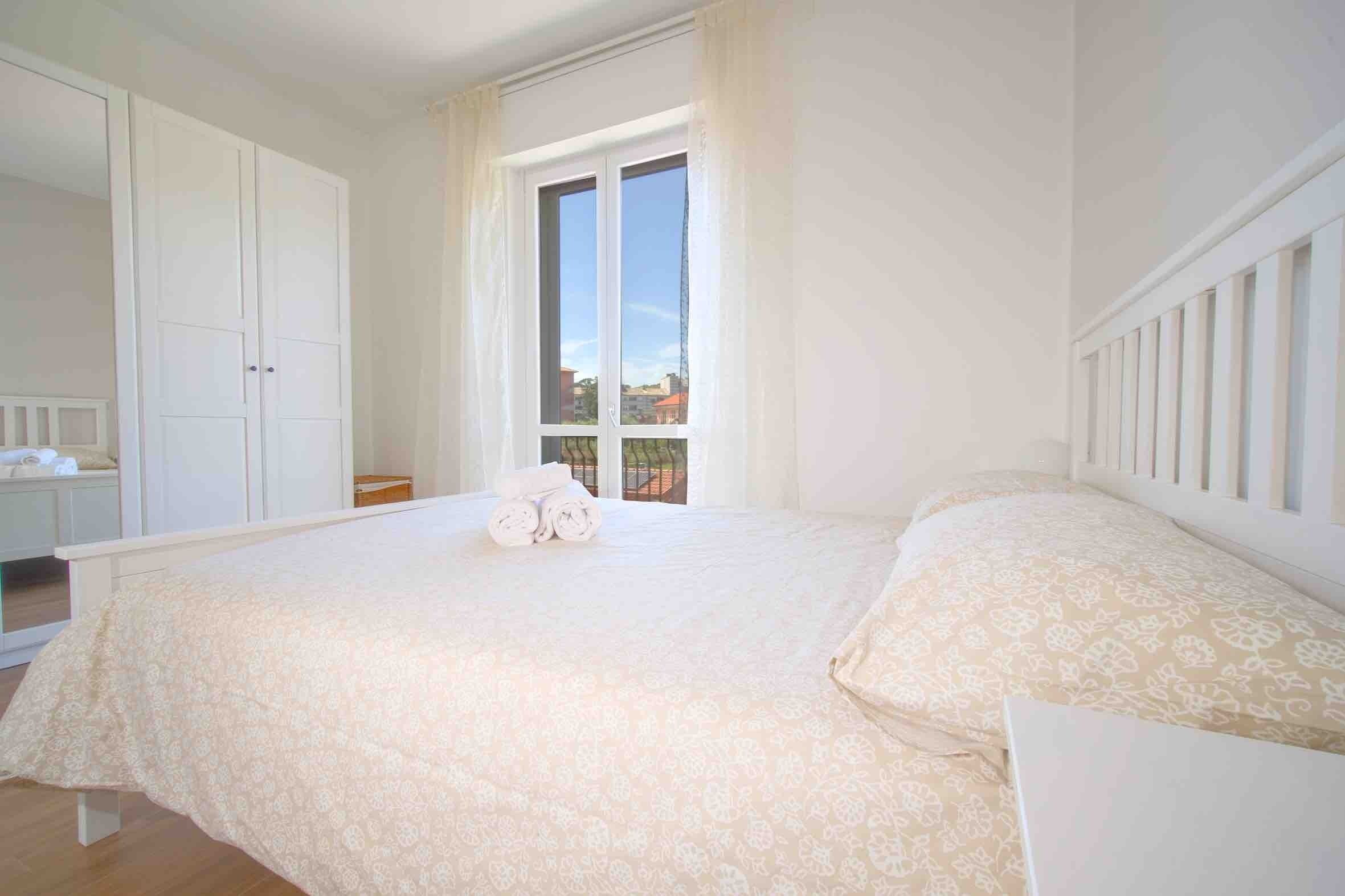 A bedroom with a large bed, a wardrobe, and a window with a view.