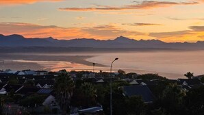 A coastal residential area with houses, a streetlight, and a view of the ocean at sunset.
