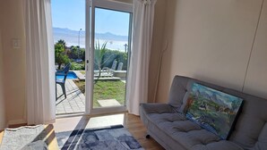 A living room with a grey sofa, a painting, and a view of a pool and mountains through a glass door.