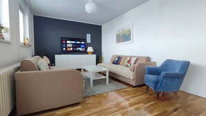 A modern living room with a beige sofa, a blue armchair, a white coffee table, and a flat-screen TV mounted on a dark wall. - One bedroom apartment with panoramic view of Zagreb (Zagreb)