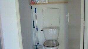 A small bathroom with a toilet, a mop, and cleaning supplies on a shelf. - T2 rez de Jardin 50m2 Bord de mer (Frontignan plage)