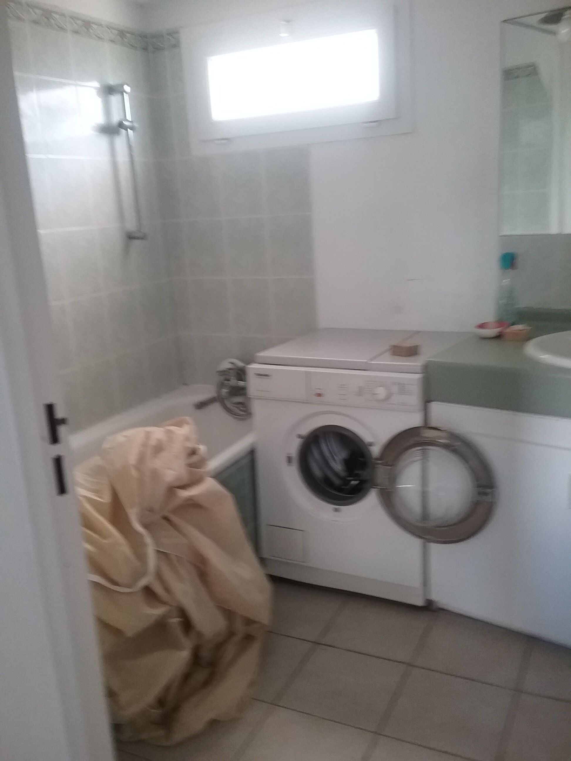 Pieni pyykinhuoltotila, jossa on pesukone ja kuivausrumpu. Kuivausrumpun yläpuolella on ikkuna, ja ovenkahvassa roikkuu pyyhe.