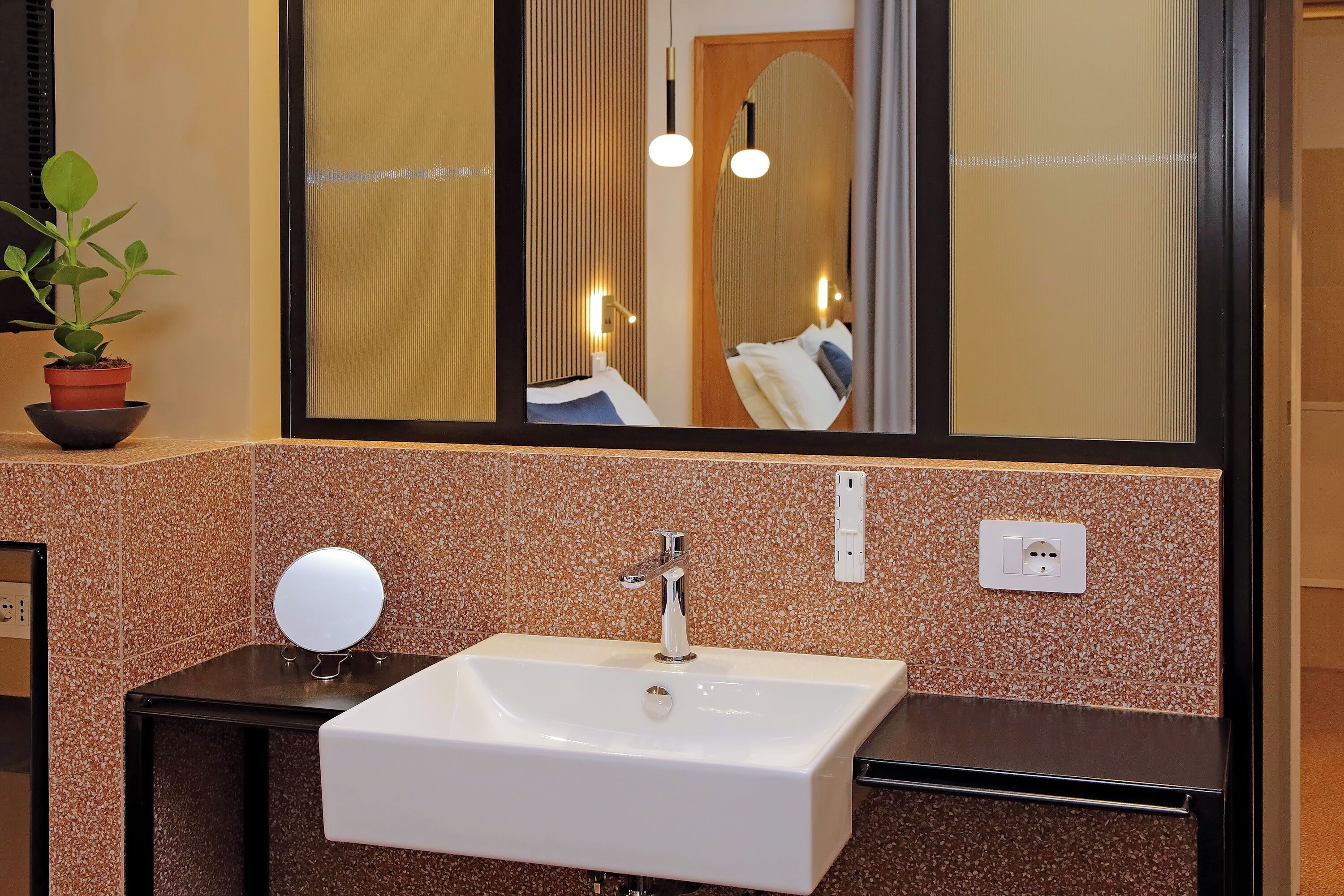 A bathroom with a white sink, a mirror, and a potted plant.