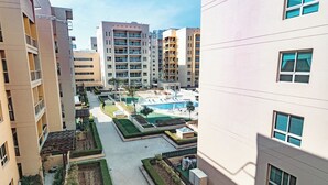 Un immeuble résidentiel à plusieurs étages, doté de balcons et d’une cour intérieure avec une piscine et des chaises longues.