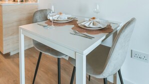 Une cuisine moderne avec une table à manger pour deux personnes, comprenant une table blanche, des chaises grises et une œuvre d’art encadrée accrochée au mur.